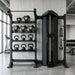 A black TORQUE multi-functional home gym cable machine paired with a matching multi-tier weight rack holding dumbbells and kettlebells, set in a modern concrete-floored gym.