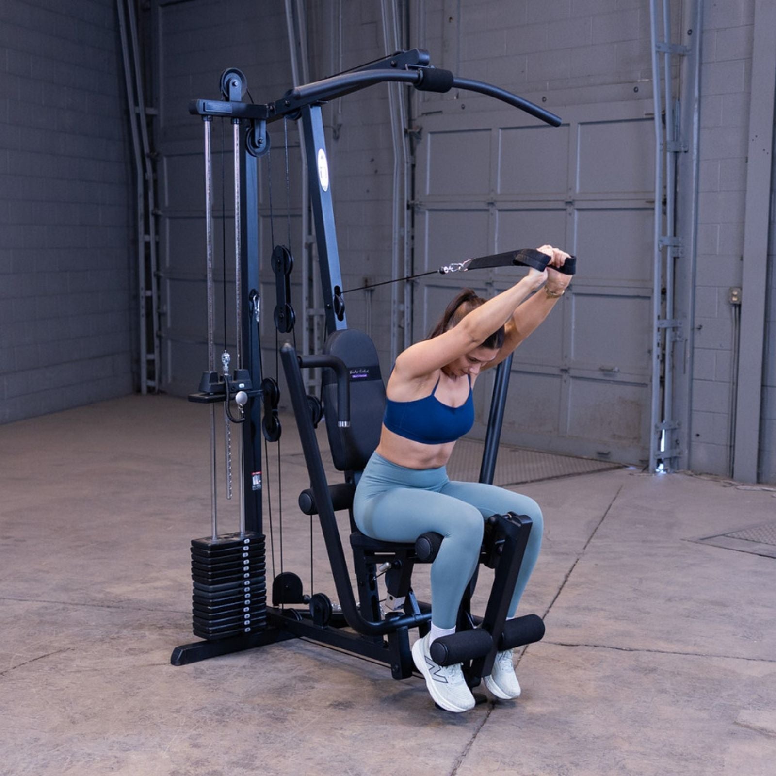 Woman performing a cable ab crunch using the high pulley and ab straps on the Body-Solid G1S Multi-Station Gym to isolate the core