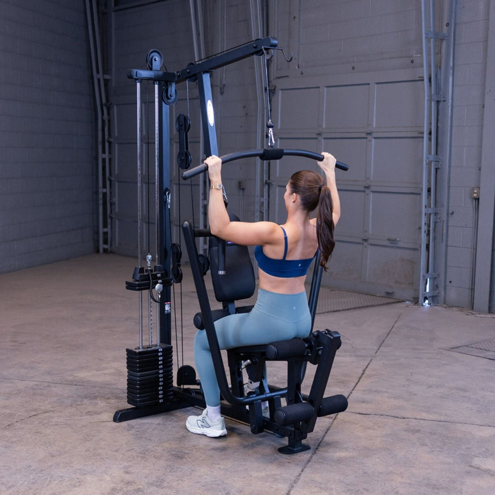 Woman performing a lat pulldown on the Body-Solid G1S Multi-Station Gym using the high pulley and wide grip bar to target the upper back