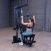 Woman performing a lat pulldown on the Body-Solid G1S Multi-Station Gym using the high pulley and wide grip bar to target the upper back