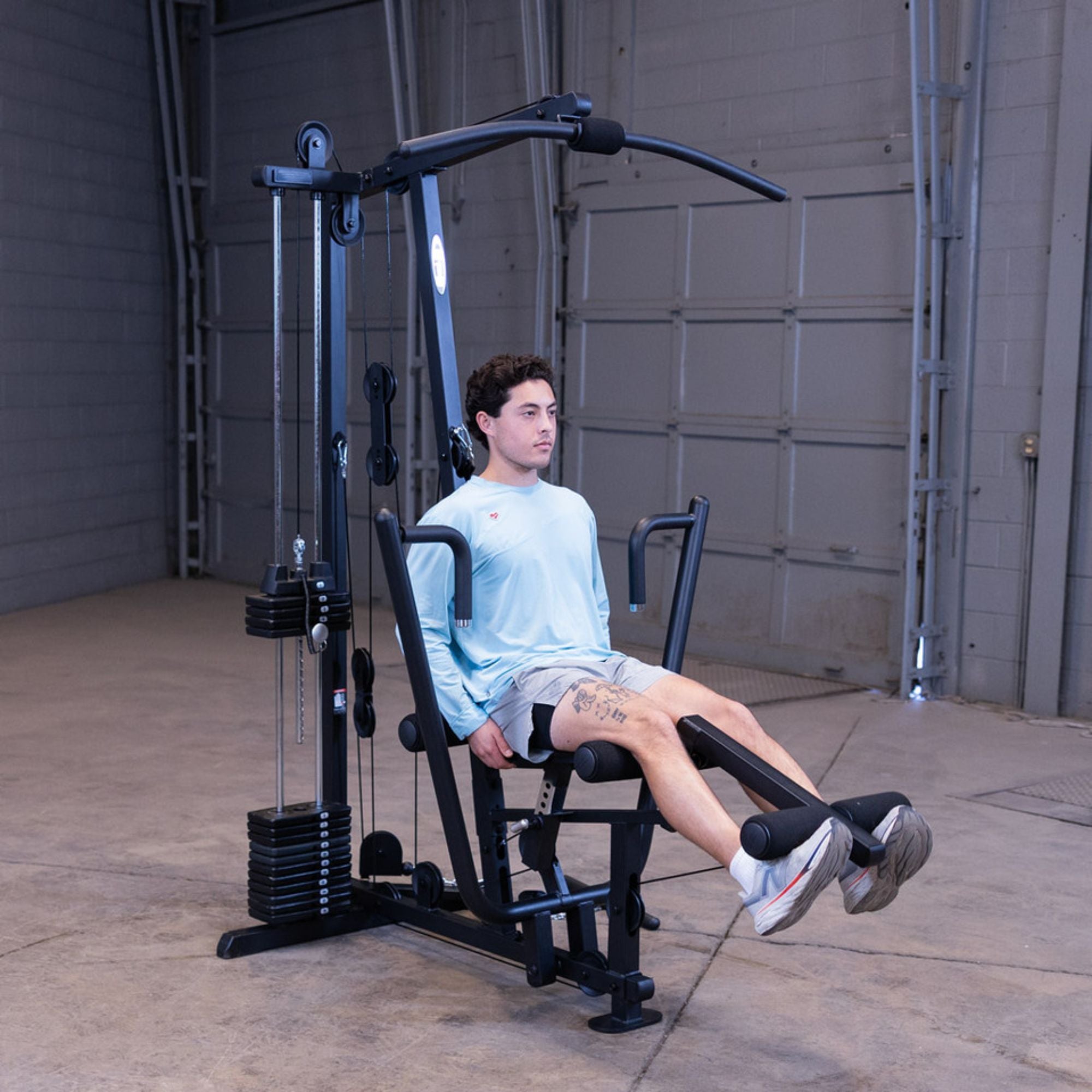Man performing a leg extension exercise on the Body-Solid G1S Multi-Station Gym in a home garage gym setting