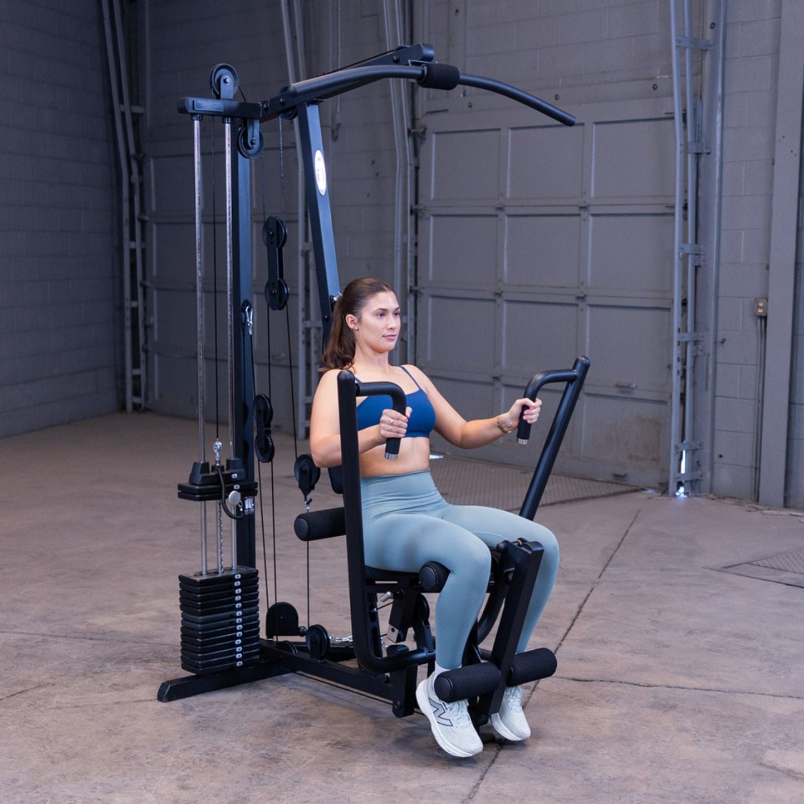 Woman performing a seated chest press on the Body-Solid G1S Multi-Station Gym using the press arm station to target chest and triceps