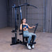 Woman performing a seated chest press on the Body-Solid G1S Multi-Station Gym using the press arm station to target chest and triceps
