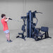 Body-Solid G9B dual stack home gym with user performing adjustable high pulley cable exercise
