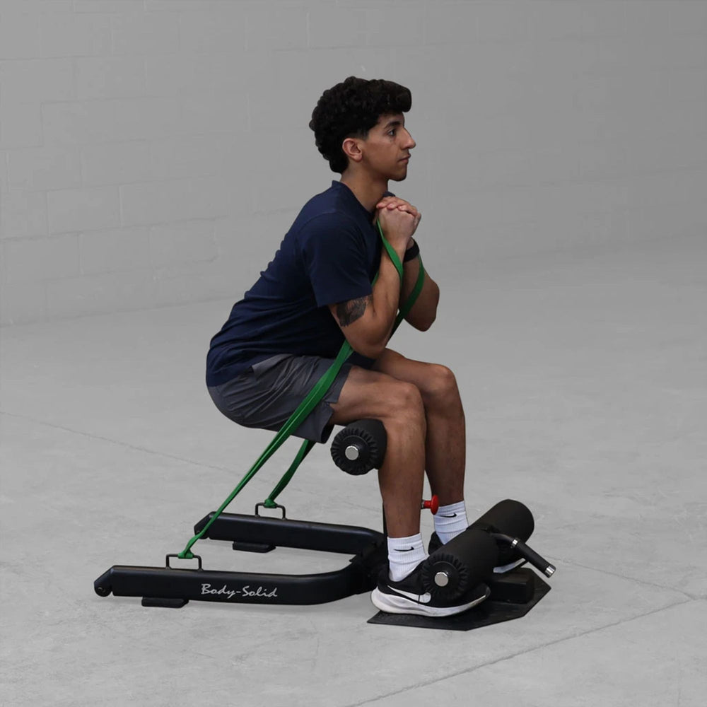 Man performing sissy squat on Body-Solid GSS50B with resistance band assistance