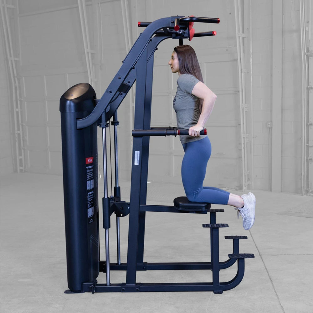 S2ACDX Series 2 Weight Assist Vertical Knee Raise Woman exercising on a black cable machine in a gray studio setting