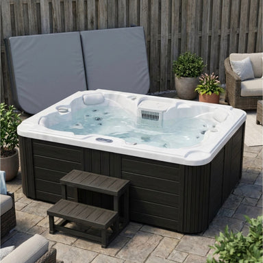 Luxury Spas Tahoe 4-Person 120v 240v hybrid Hot tub with steps on a patio area with outdoor furniture and plants.